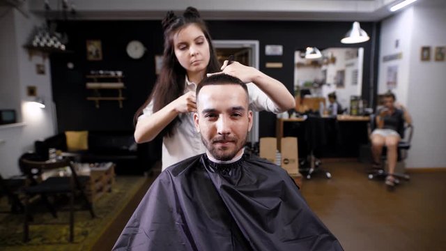 Woman making haircut to stylish handsome client sitting in barber salon