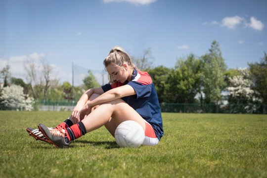 Soccer player sitting with ball on playground