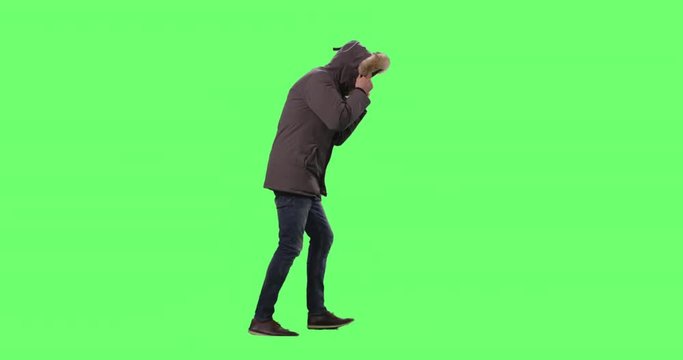 Man in a Wearing Winter Jacket with Hood On Walks Against Cold Weather and Strong Wind. Shot on a Mock-up Green Screen Background.