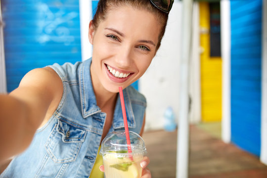 Lovely young smiling woman drinking lemonade and make a selfie.