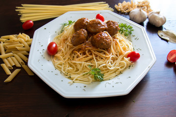 Delicious and tasty italian spaghetti with meatballs served on plate with tomatoes in the background
