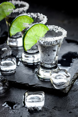 Silver tequila shots with ice and lime on black table background