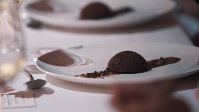Female hand with red nail polish take metal fork and piece of chocolate dessert of white plate in luxurious restaurant