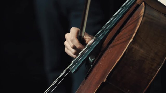 Unrecognisable male hand hold fiddlestick finger pulls string of cello playing music in dark room, close up