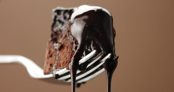 piece of chocolate cake on a fork closeup with slow liquid toping pouring on
