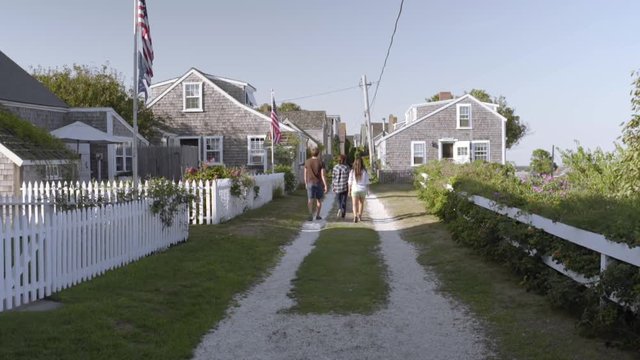 Teens Walk Down Shell Road, Lined With Cottages And American Flags, In New England Seaside 