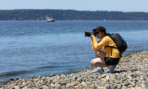 Woman nature photographer working on photos near shoreline of ocean