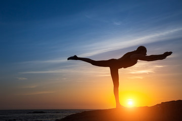 Silhouette of woman doing fitness exercise on the sea beach during amazing sunset.