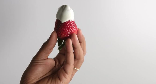 man's hand pulling up holding a strawberry with cream