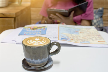 Young beautiful Asian woman planning her trip around the world by searching the data to travel with the map on the wooden table at the cafe