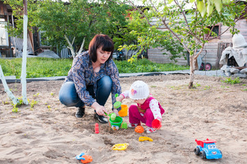 Brunette mom playing with her baby in the sandbox