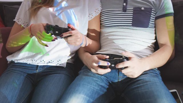 Close up shot of woman and man hands who playing video game while sitting on sofa.