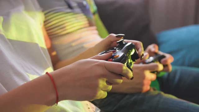 Close up shot of couple hands who playing video game while sitting on sofa. Side view.