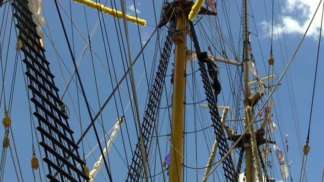 Masts, rigging, banners and pirate flag waving in wind on Indonesian tall ship Dewaruci against blue sky   