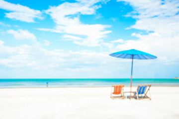 Blurred image of beach chairs and parasol on white sand beach in summer blue sky background