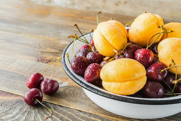  Fresh ripe apricots and cherries in a white bowl on the kitchen table