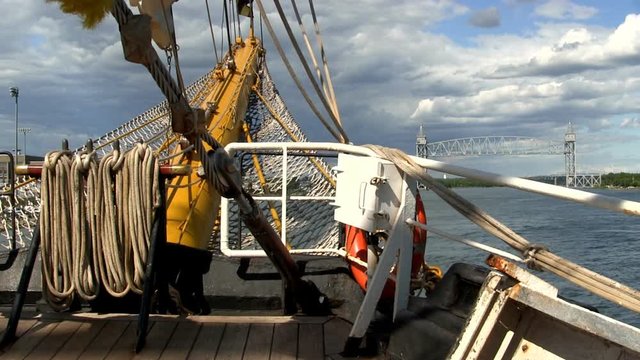 Bow of tall ship Dewaruci from deck looking out toward bowsprit with Cape Cod canal and train bridge in distance