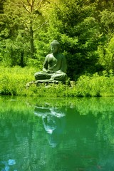 Buddha statue  on the shore of a pond with reflection