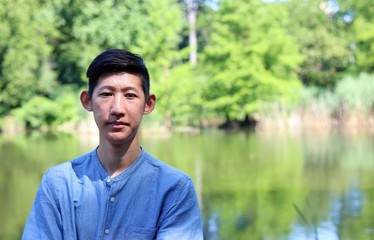 Close up portrait of young handsome asian man standing by scenic wildlife nature pond waterfront