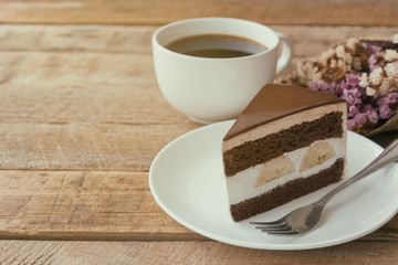 Banana chocolate cake on white plate served with black coffee. Chocolate cake layered with whipped cream and banana look so delicious. Enjoy eating at cafe restaurant with chocolate cake and coffee.