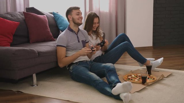 Emotional young couple eating pizza and playing video game at home.