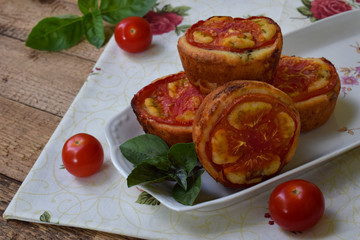Salty snack. Homemade muffins with cheese, tomatoes and basil on wooden background. Savory pastry.