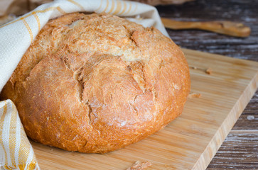 Fresh baked loaf of bread  with linen napkin on cCrumbsutting board.Rustic style food background.
