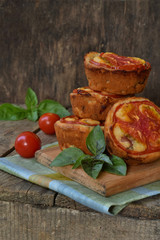 Salty snack. Homemade muffins with cheese, tomatoes and basil on wooden background. Savory pastry.
