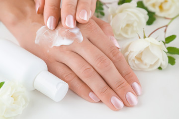 Hands moisturizing cream cares about woman's hands skin. Manicure beauty salon. Spring and summer gentle atmosphere with fresh and fragrant white roses on the table.
