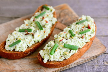 Avocado guacamole toast on a cutting board and vintage wooden table. Rye toast with guacamole sauce, fresh green onion and spice. Simple breakfast idea. Closeup