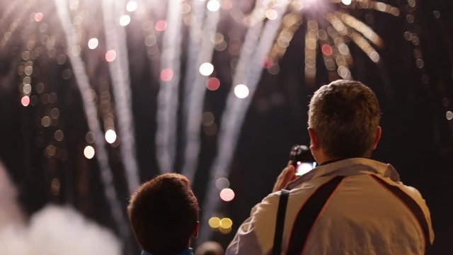 Unrecognizable father and son filming and watching fireworks