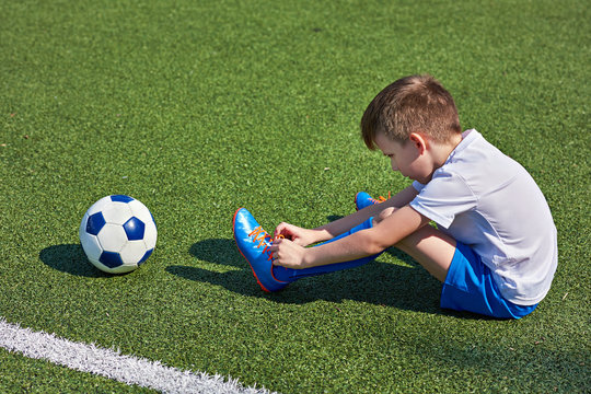 Boy football soccer tying laces him boots on grass