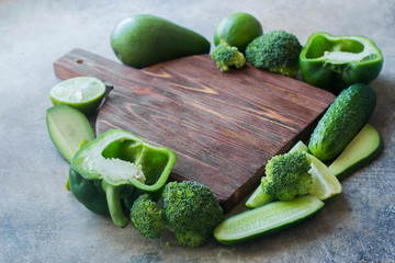 Food background. Variety green vegetables around wooden board. Top view of group vegan product - pepper, avocado, broccoli, cucumber, lime. Healthy food concept. Copy space