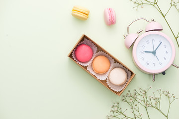 French macaroons. Many variegated sweet macarons in box with bouquet of pink roses on the table