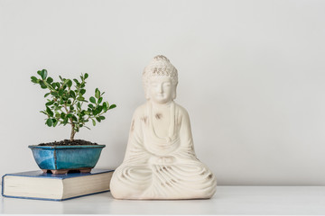Buddha ornament on white background with book, bonsai tree & copy space for text.