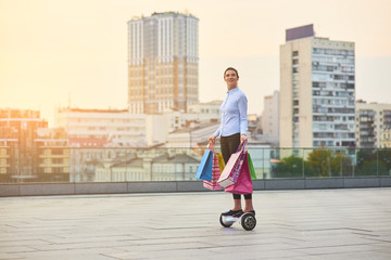 Woman on hoverboard, shopping bags. Young female on city background.