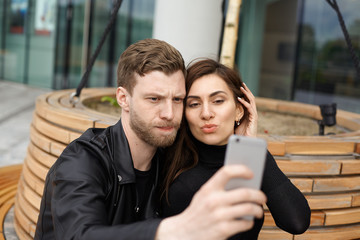 People, modern technology, lifestyle and relationships. Fashionable European couple in black clothing taking selfie using electronic gadget while chatting online with friends via messaging service