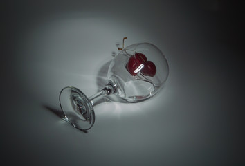 closeup on a white background lies a glass with cherries and water.