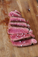 Beef steak is sliced on a wooden board. Sprinkled with coarse salt