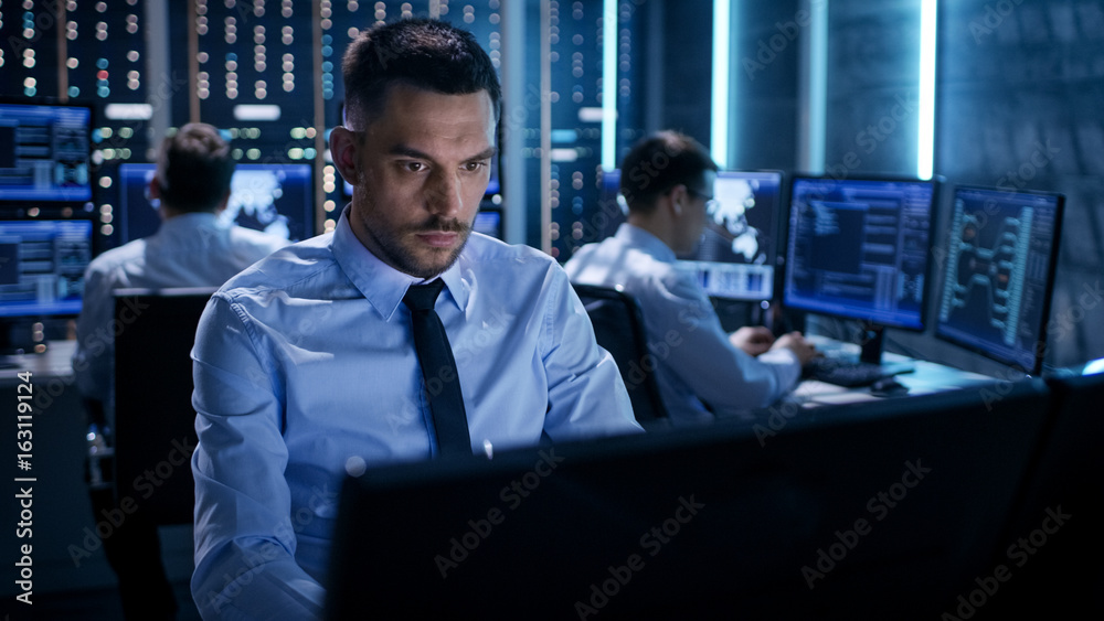 Poster Close-up of Technical Engineer Working on His Computer With Multiple Displays in Monitoring Room. In the Background His Colleagues with Graphics and Various Data on Their Monitors.