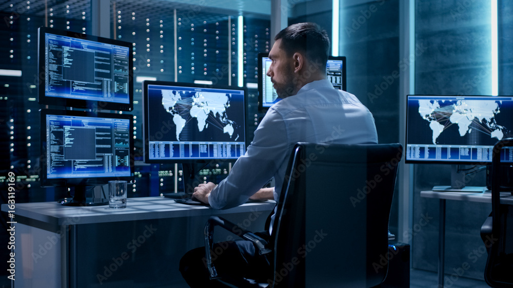 Poster Technical Controller Working at His Workstation with Multiple Displays. Displays Show Various Technical Information. He's Alone in System Control Center.