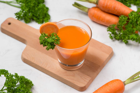 Glass of fresh carrot juice with vegetables on table.