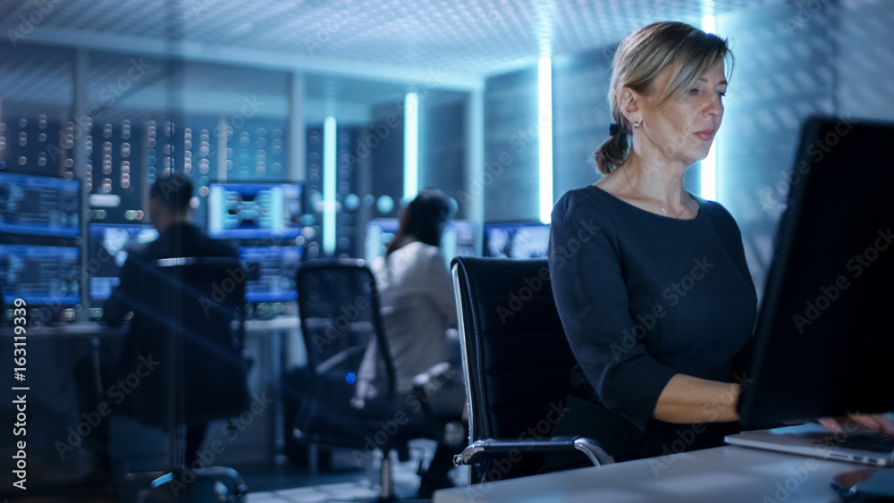 Poster female it engineer works on her desktop computer in government surveillance agency. in the backgroun