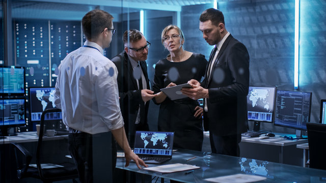 Team Of Corporate Managers Having Meeting In Monitoring Room. They're In State Of The Art Facility. Computers Have Animated Screens.