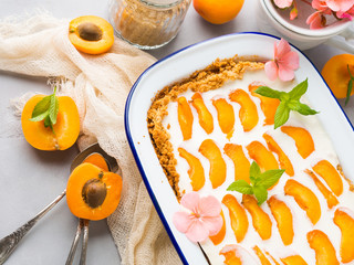 Home made apricot not baked cheese cake in enamel tin on gray background with flowers