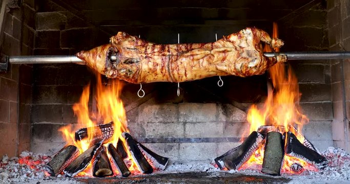 pig spinning on spit - cooking piglet in firewood grill