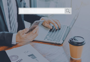 Business man using laptop and smartphone with blank search bar at office space background -...