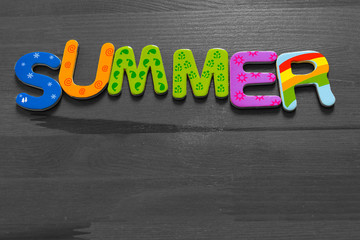 The word Summer written in cheerful warm letters from a magnet on a brown wooden table. Black and white. With place for copyspace