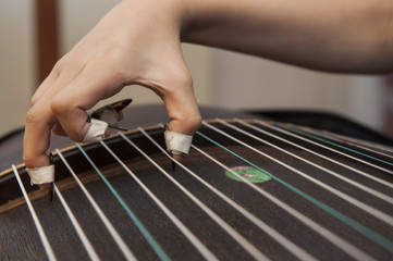 A girl is playing Guzheng.The guzheng or gu zheng, also simply called zheng, is a Chinese plucked zither. It has 18 or more strings and movable bridges.