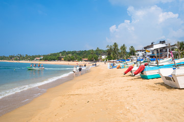 Fototapeta na wymiar At the beach of one of the major tourist spots in the south west of Sri Lanka. Tourist do sunbathing and aquatic sports. Outrigger and traditional fishing boats on the beach